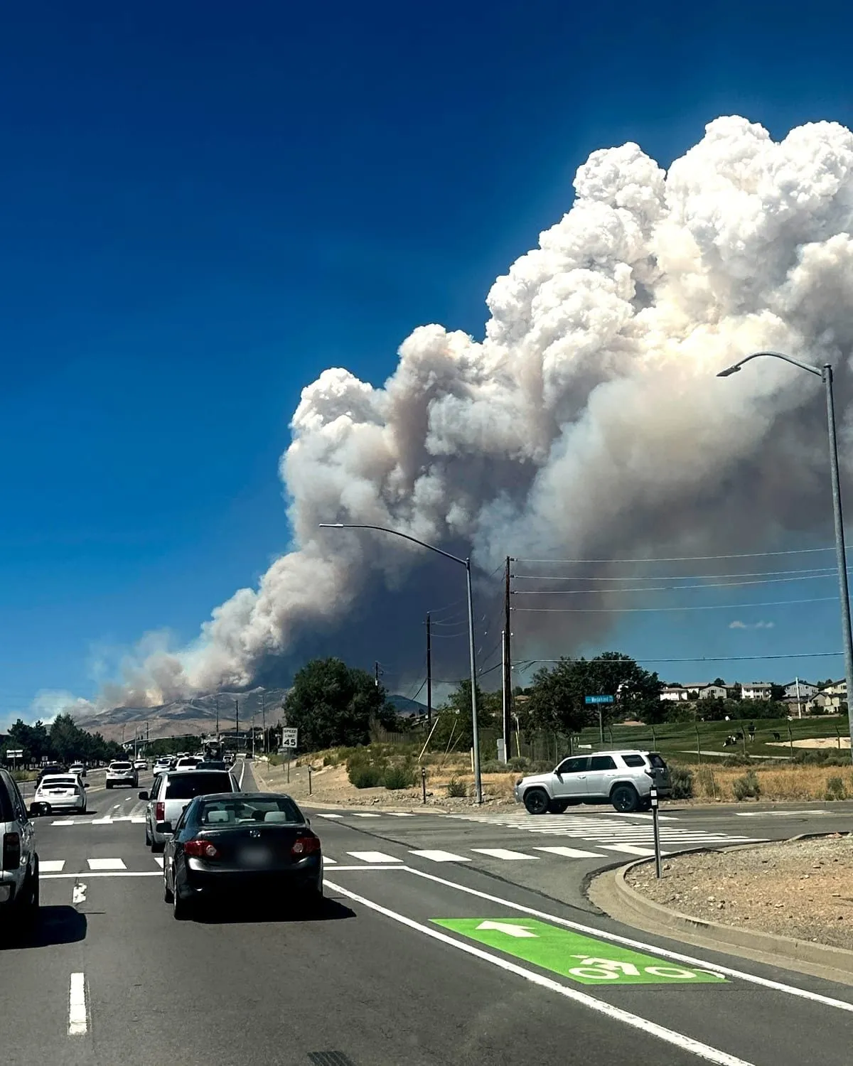 A towering wildfire smoke plume rising over the hills beyond a northern Nevada road