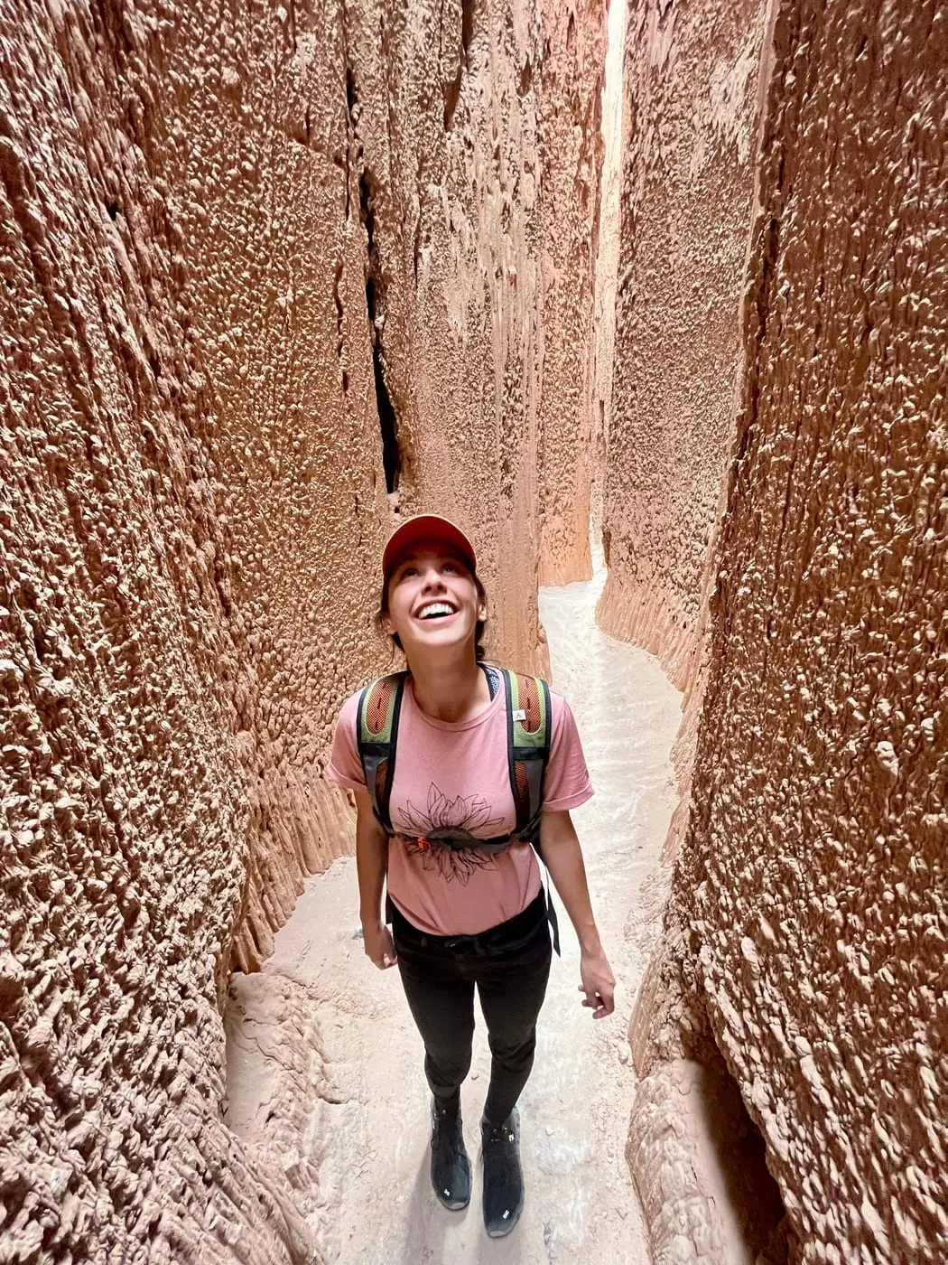 Erica grinning up at the walls of a narrow red slot canyon