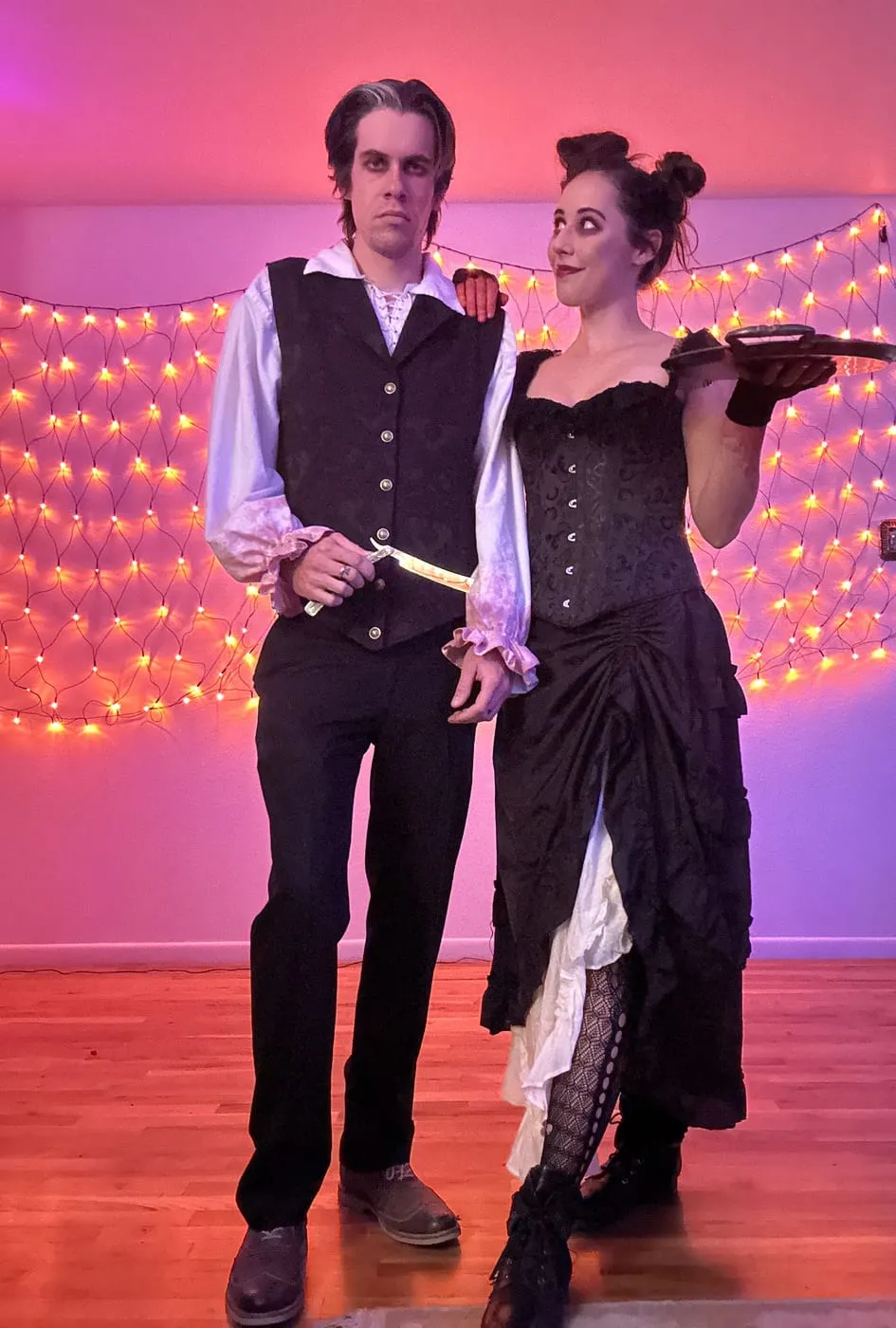 Erica and her partner in Victorian costume under a wall of string lights