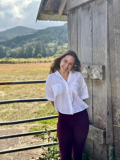 Erica Gallegos smiling beside a weathered barn, green mountains behind her