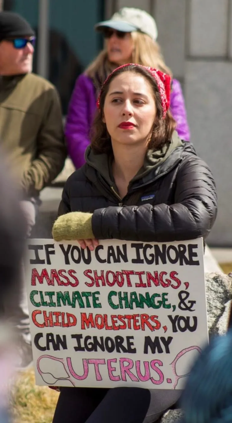 Erica at a rally with a sign: If you can ignore mass shootings, climate change, and child molesters, you can ignore my uterus